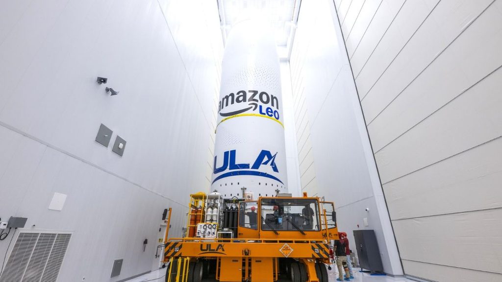 Amazon Leo avanza verso il primo lancio Vulcan: 40 satelliti trasferiti alla VIF-A 1 Fairing Amazon Leo con logo ULA su un trasportatore industriale all'interno di una struttura di integrazione