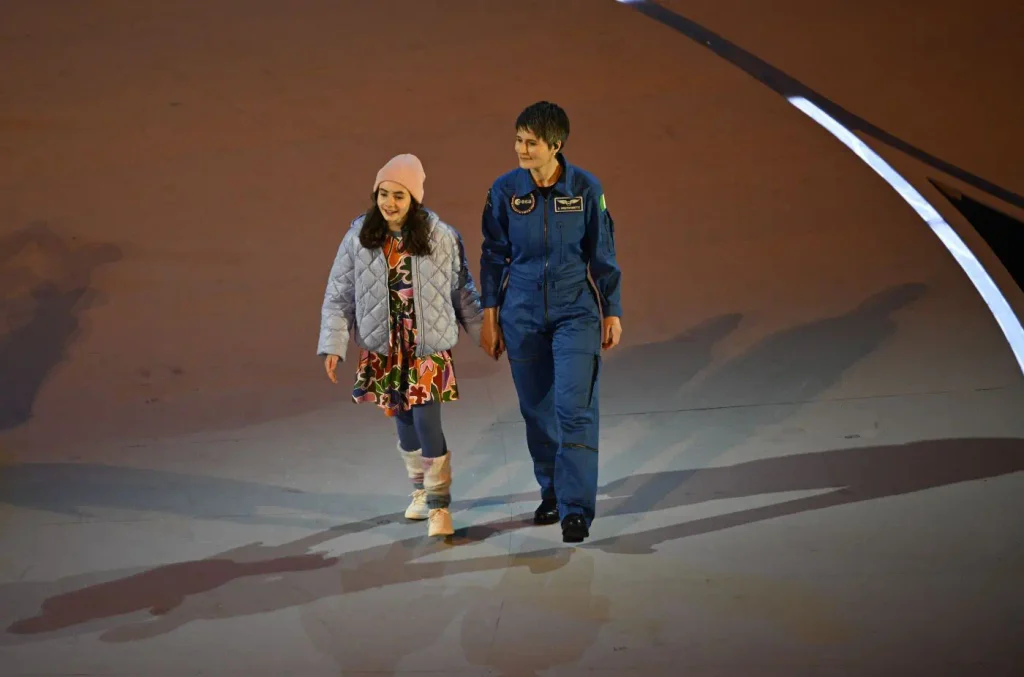 Il futuro dello spazio ha bisogno del talento delle donne 1 Samantha Cristoforetti in tuta da astronauta ESA cammina accanto a una ragazza sul palcoscenico, immagine simbolo dei temi di Donne fra le Stelle.